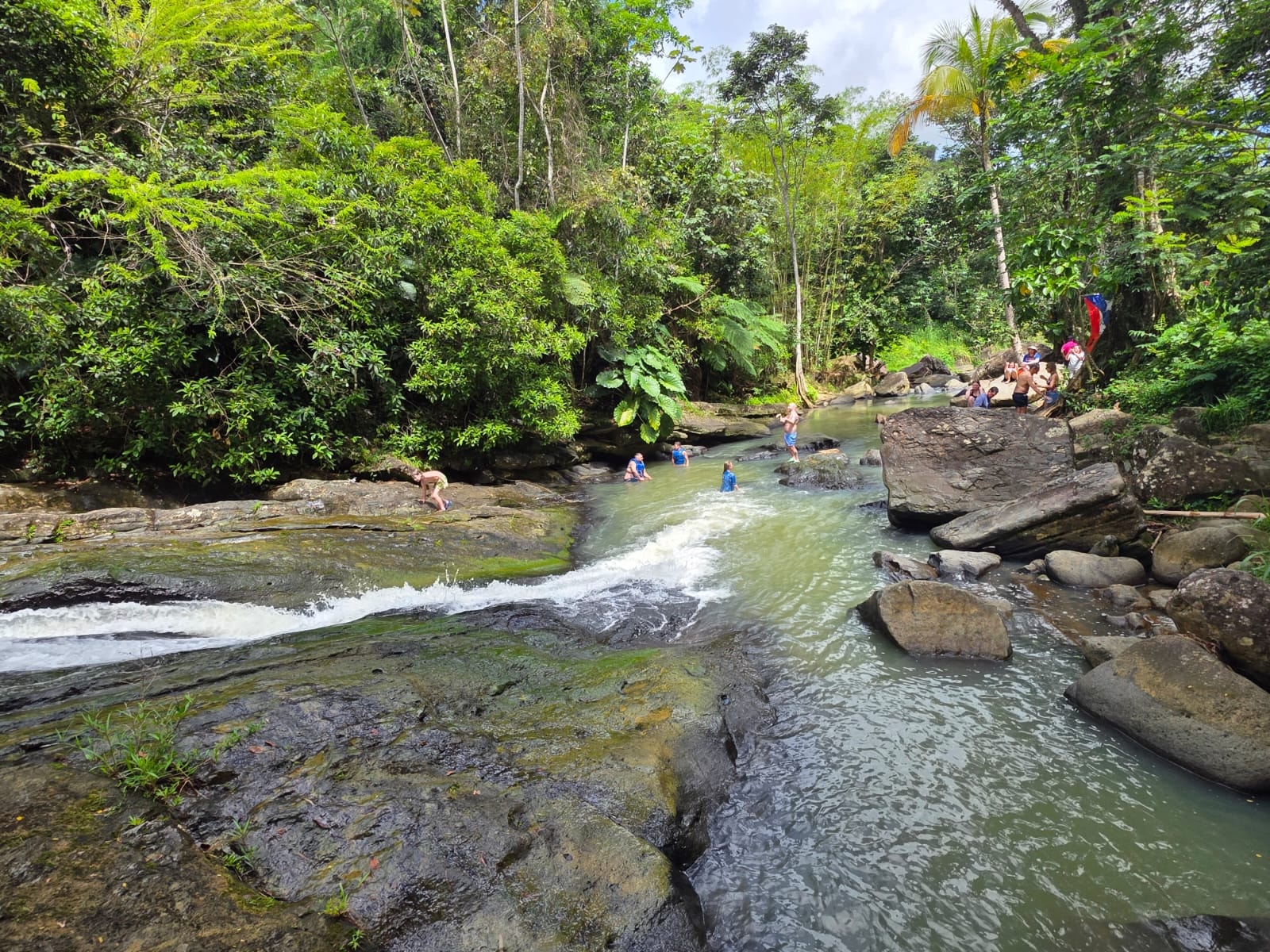 Guests sliding down natural rock waterslides and swimming in the crystal-clear river at El Yunque