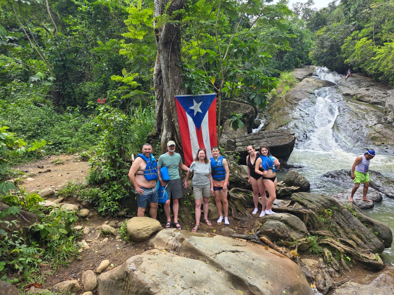 Group of guests posing proudly with the Puerto Rico flag in front of a stunning jungle waterfall